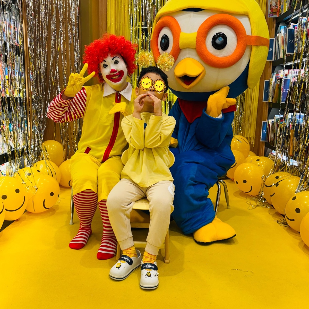 옐로 데이 장식 앞에서 캐릭터와 함께 사진을 찍는 아이